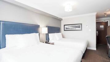 A hotel room with two beds, a headboard, a nightstand, a lamp, and a framed picture on the wall.