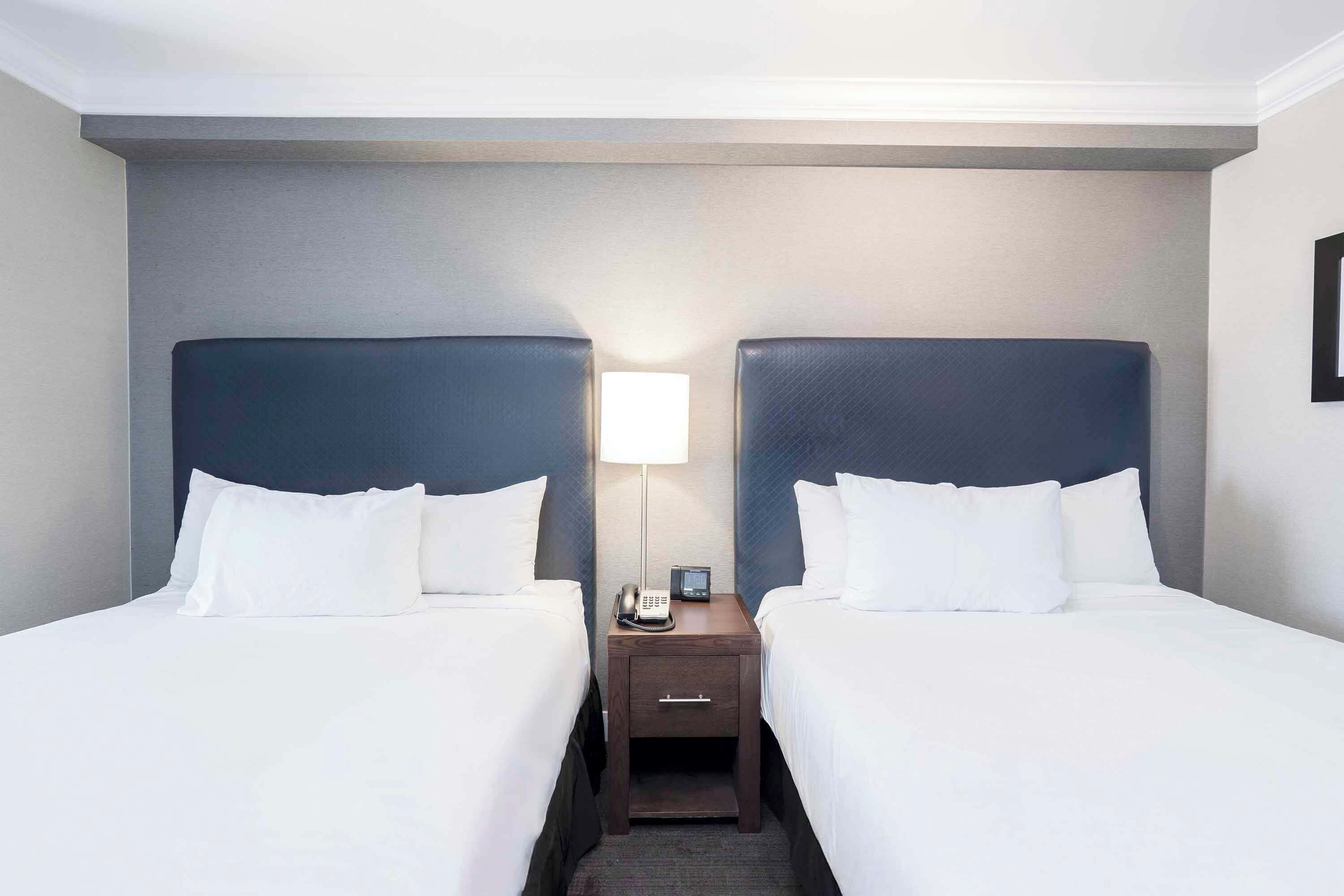 A hotel room with two beds, a nightstand with a lamp, and a phone.