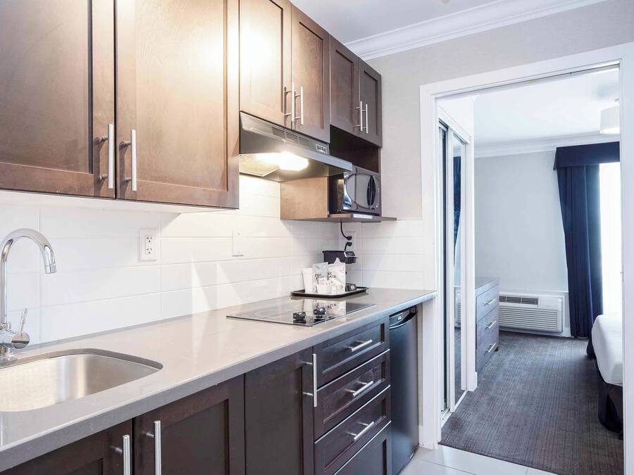A compact kitchen with a stainless steel sink, dark wooden cabinets, a microwave, and a small countertop.