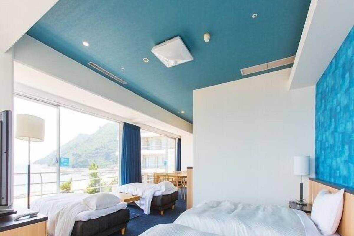 Ein Hotelzimmer mit zwei Betten, einem Schreibtisch, einem Fernseher und einem großen Fenster mit Blick auf die Berge.