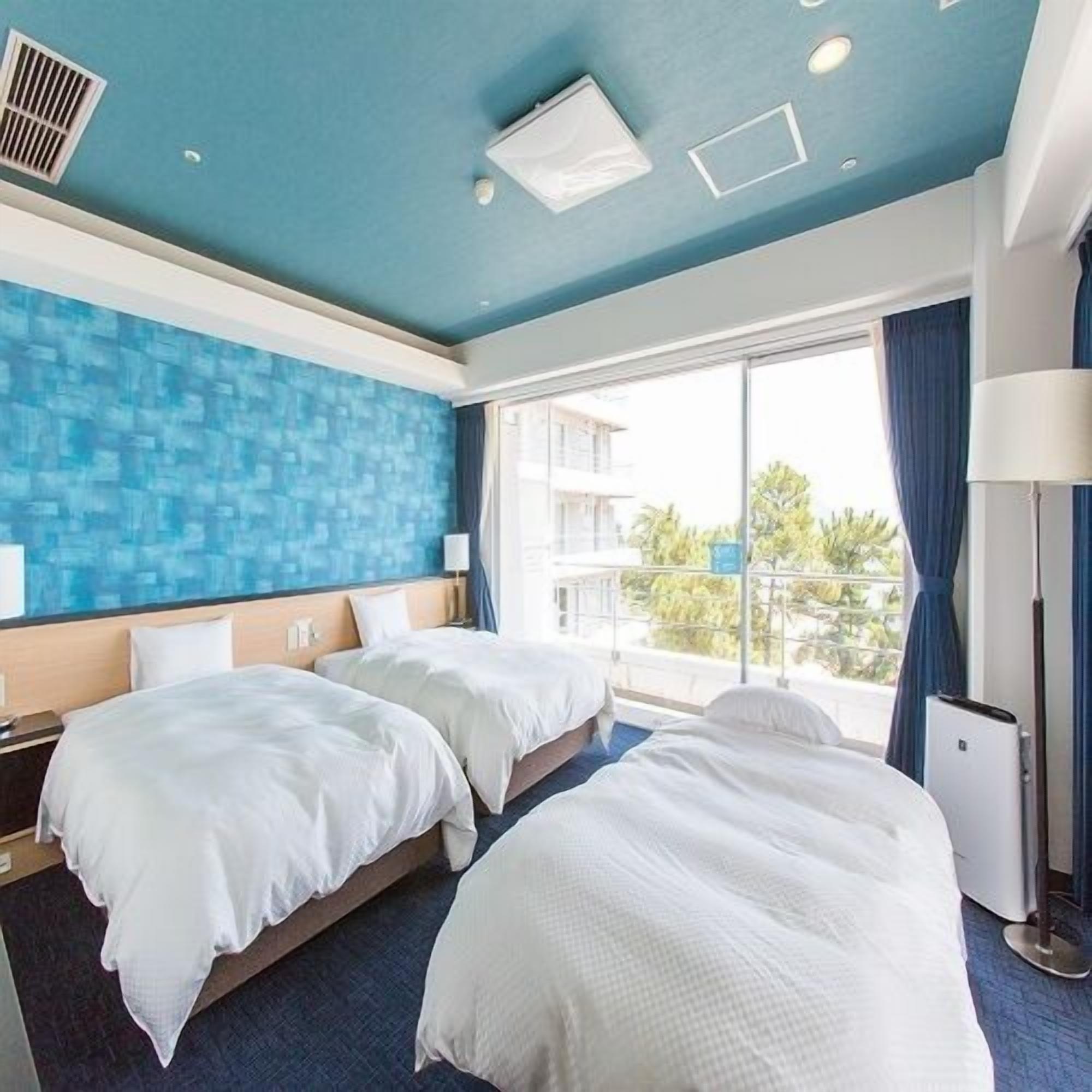 A hotel room with two beds, a large window with a view, and a blue accent wall.