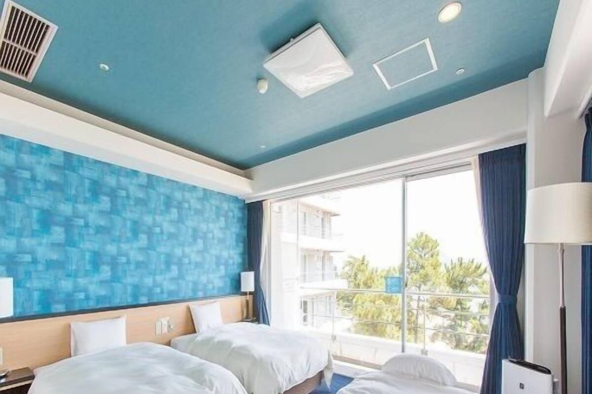 Ein Hotelzimmer mit zwei Betten, einem großen Fenster mit Ausblick und einer blauen Akzentwand.