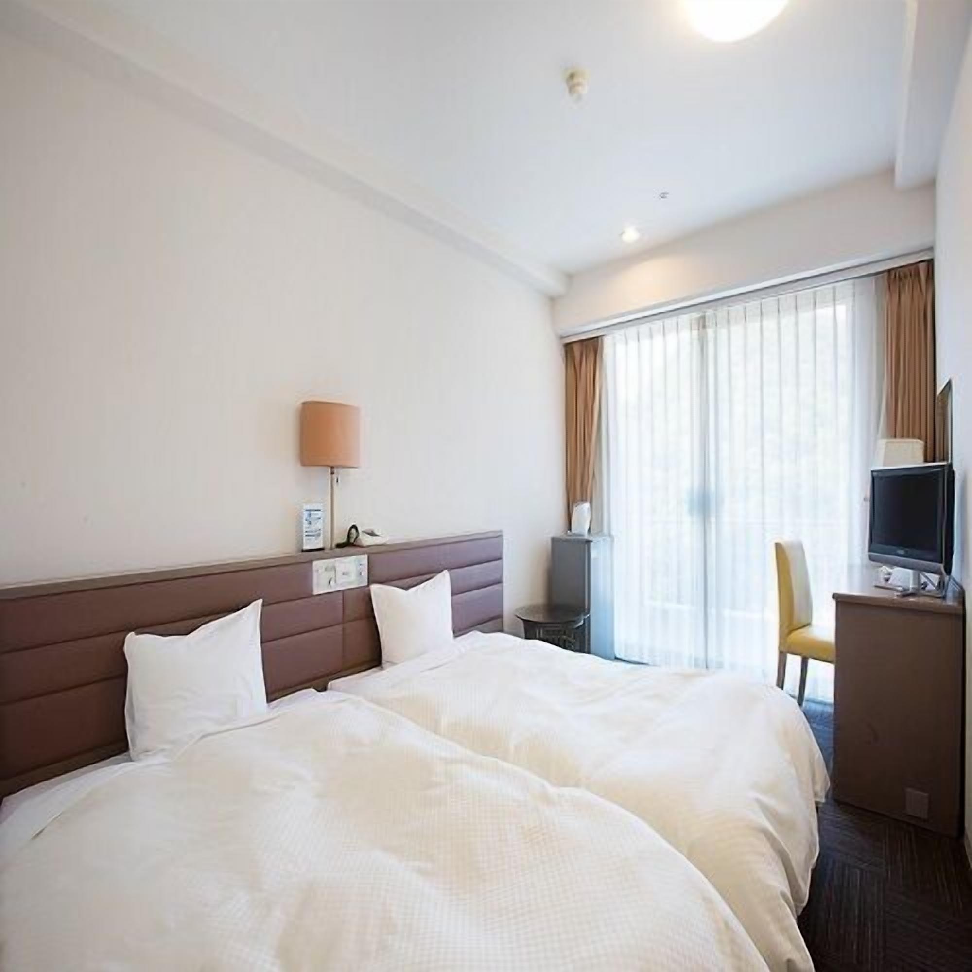 A hotel room with a bed, a desk, a chair, a TV, and a window with curtains.