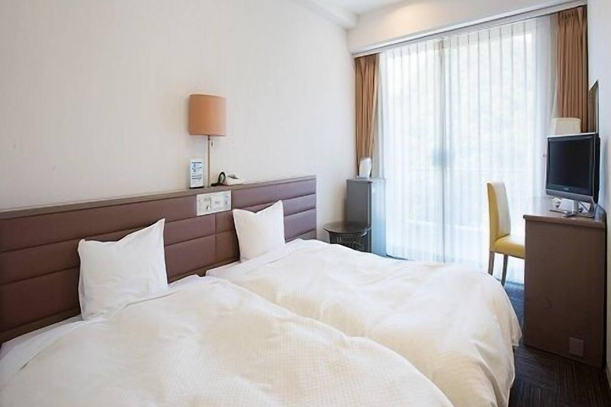 Ein Hotelzimmer mit Bett, Schreibtisch, Stuhl, Fernseher und einem Fenster mit Vorhängen.