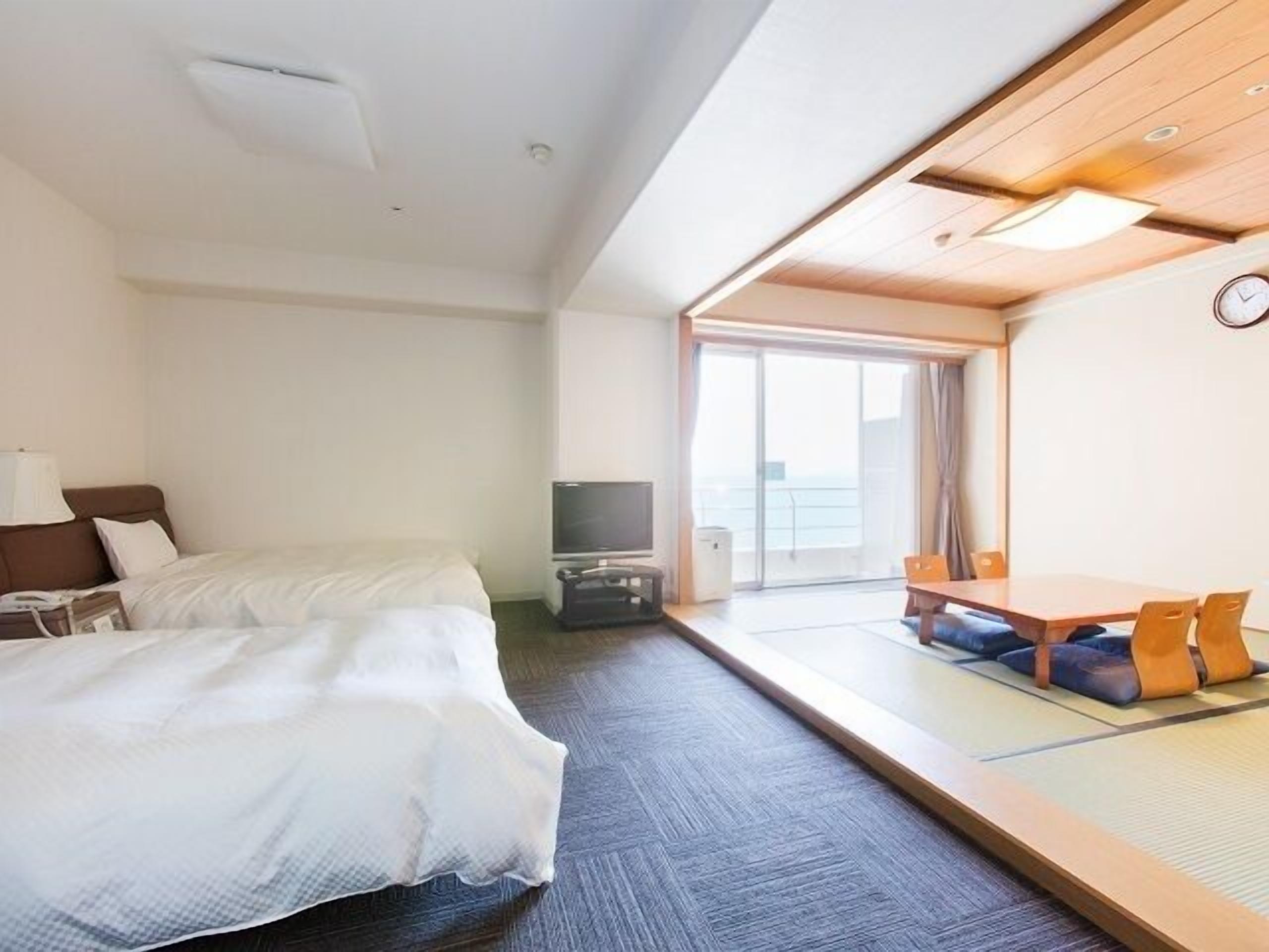 Una habitación de hotel con cama, televisión, una mesita con sillas y vistas por una ventana grande.