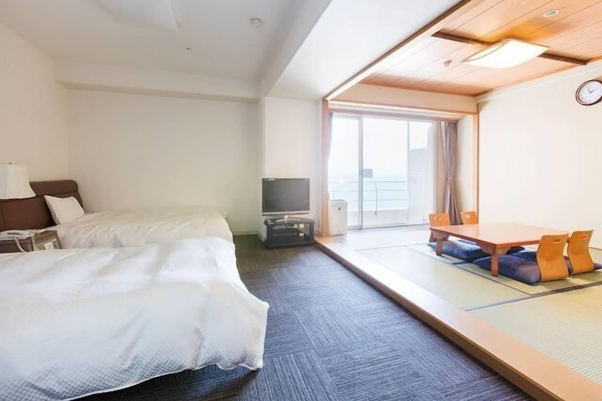 Una habitación de hotel con cama, televisión, una mesita con sillas y vistas por una ventana grande.