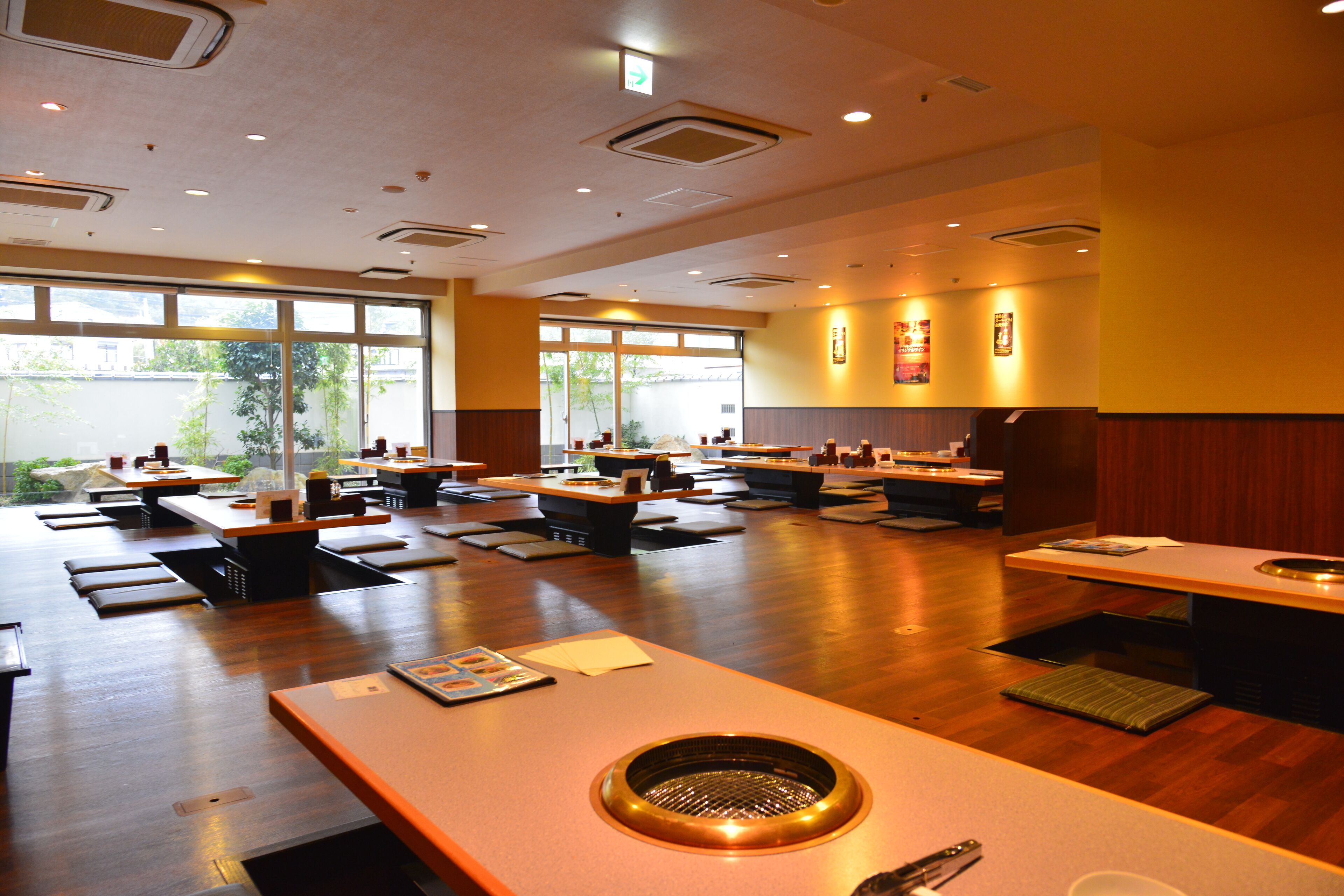 A restaurant with multiple tables and booths, large windows, and a central grill area.