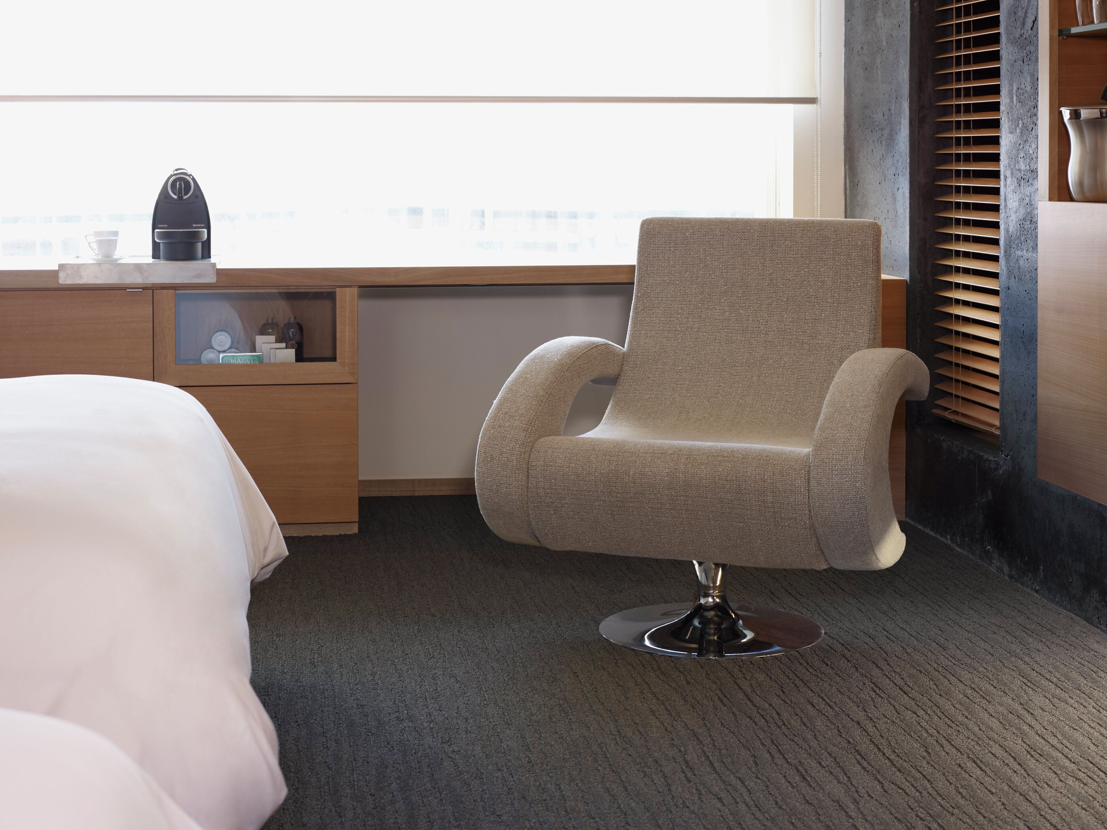 Una habitación de hotel moderna con una cama individual, un escritorio con cafetera y una ventana con persianas.