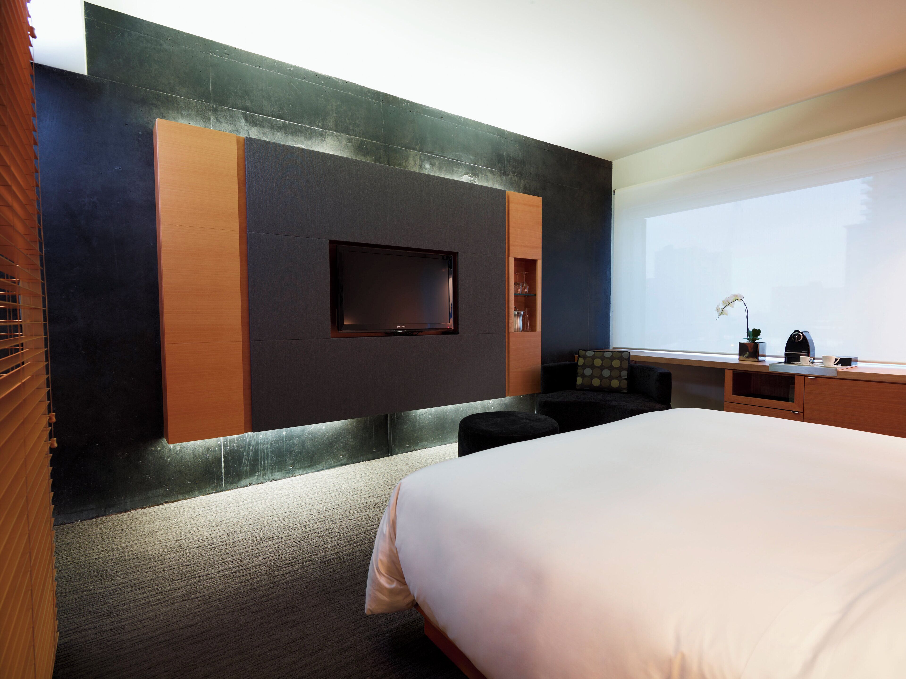 Quarto de hotel moderno com uma cama grande, televisão de tela plana na parede, escrivaninha com cadeira e janela com vista.