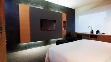 Quarto de hotel moderno com uma cama grande, televisão de tela plana na parede, escrivaninha com cadeira e janela com vista.