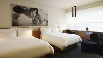 A hotel room with two beds, a desk, a chair, a coffee machine, and a large window.