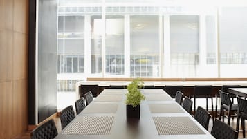 Een vergaderruimte met een lange tafel, zwarte stoelen en een plant in pot.