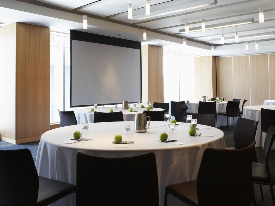 A conference room with round tables, chairs, a projector screen, and a large window.