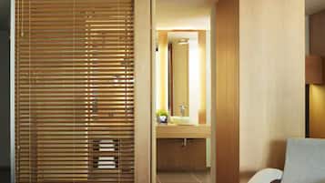 Een hotelkamer met een bed, een stoel, een houten schuifdeur en een badkamer met een wastafel en spiegel.