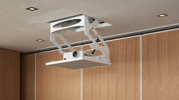 Proyector instalado en el techo de una habitación con paneles de madera e iluminación empotrada.