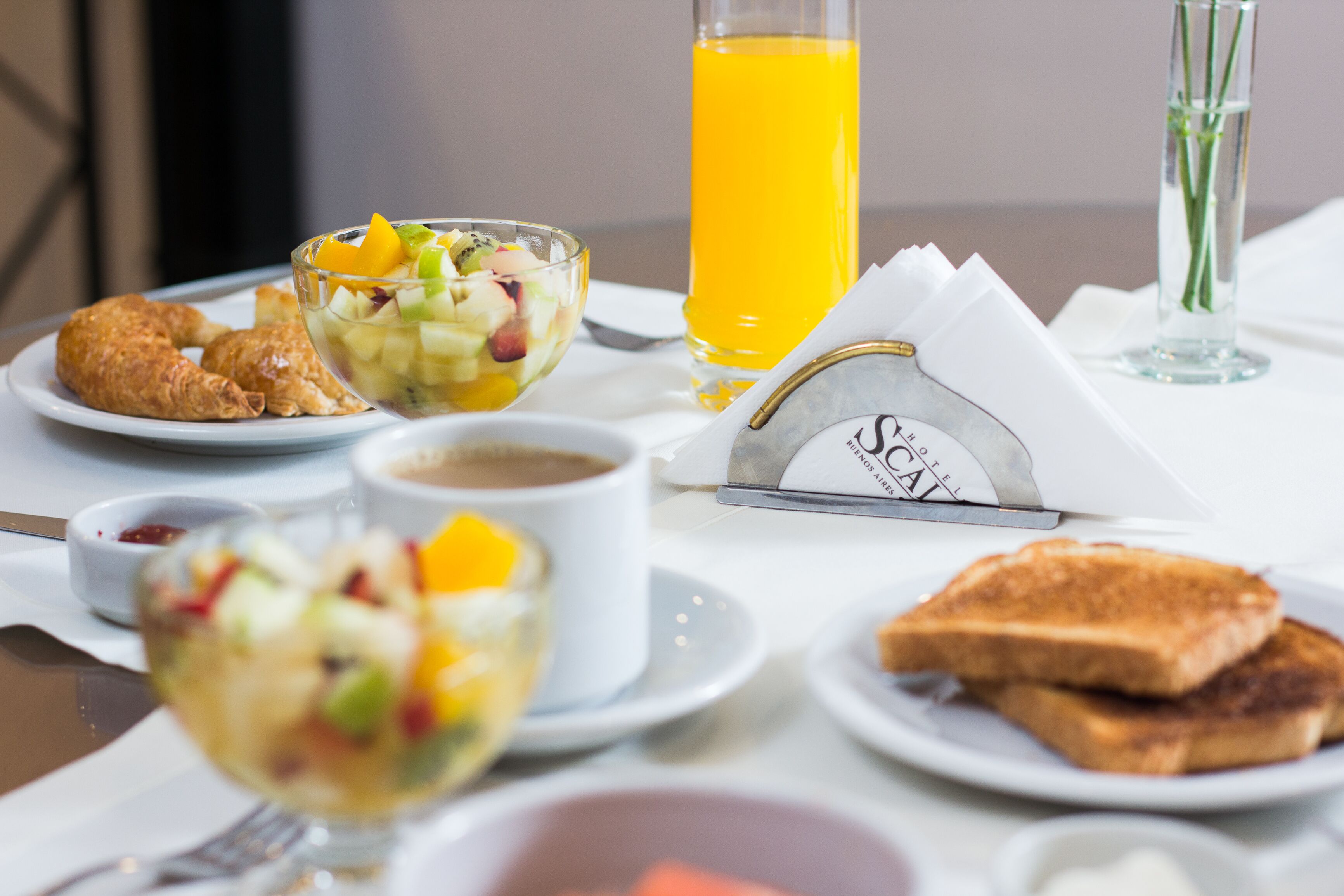 A breakfast setting with croissants, fruit salad, toast, coffee, and orange juice on a table.