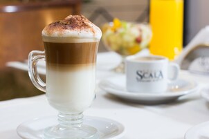 Un capuchino en una taza de vidrio transparente sobre un platito blanco.