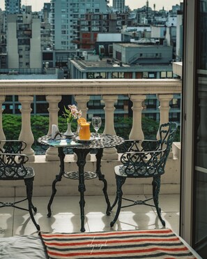 Un balcón con una mesa y sillas, un jarrón con flores, un vaso de jugo de naranja y una alfombra a rayas.