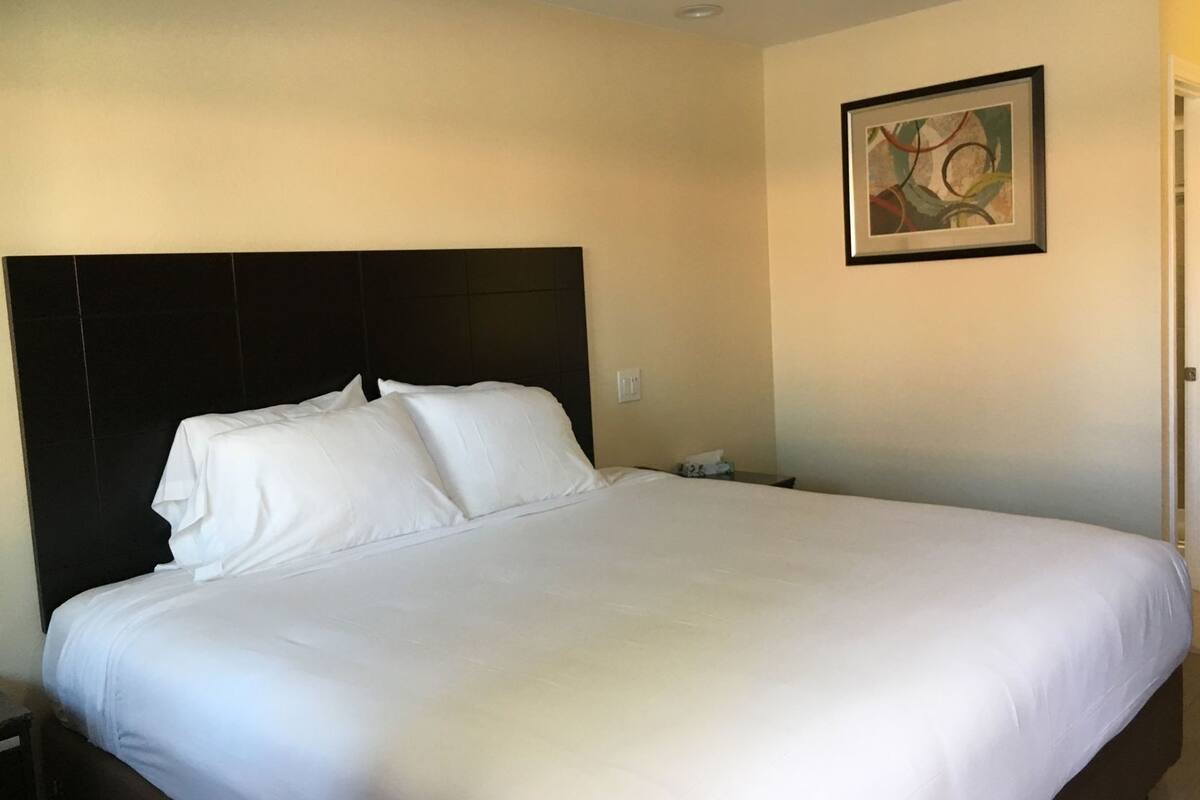 A hotel room with a large bed, a dark headboard, a nightstand, and a framed abstract painting on the wall.