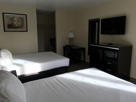 A hotel room with two beds, a desk with a lamp, a TV, and a microwave.