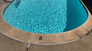 Una piscina azul cristalina con una escalera metálica y un borde de azulejos.