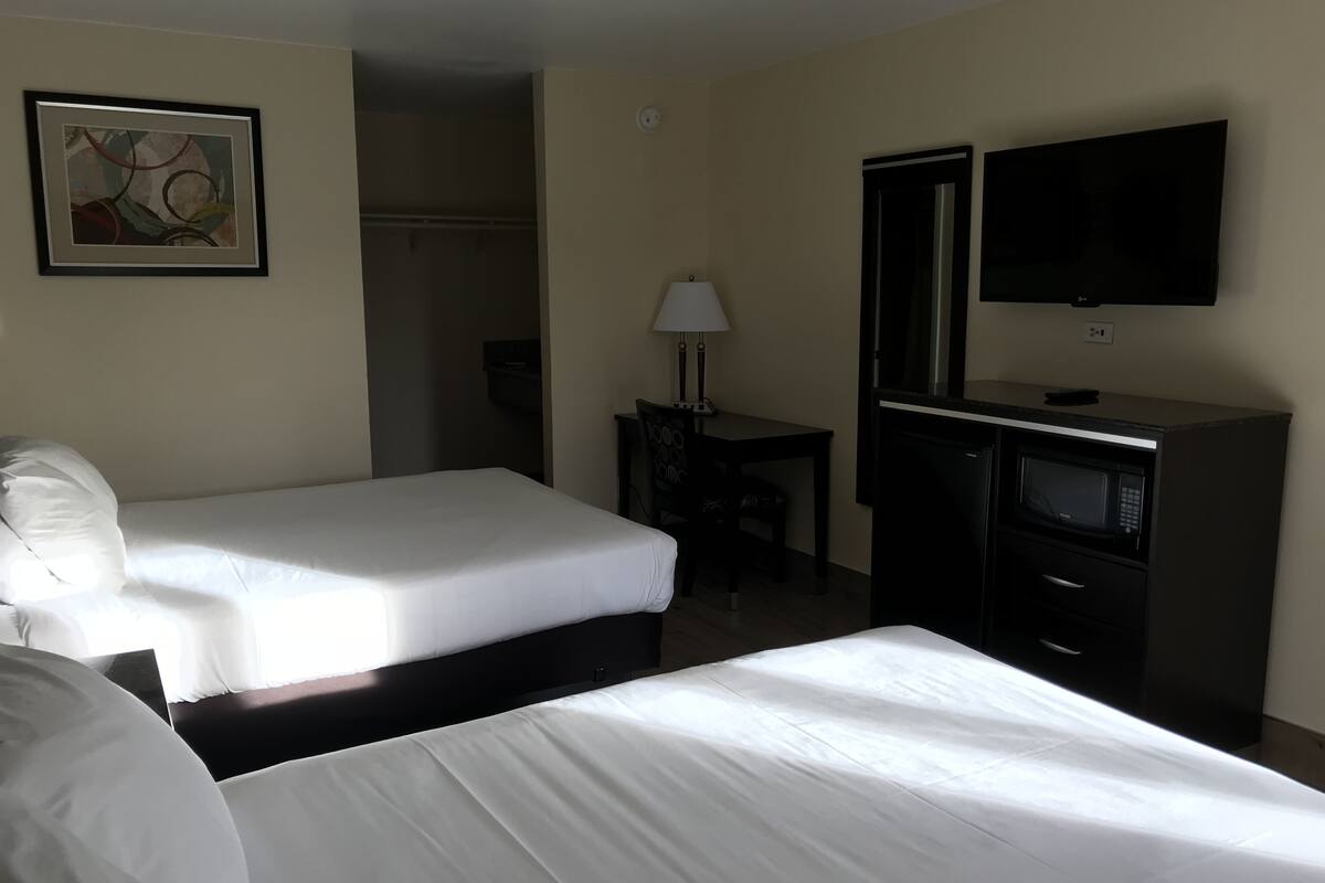A hotel room with two beds, a desk, a TV, and a microwave.