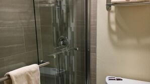 Un baño con cabina de ducha de vidrio, inodoro y toallero con toallas dobladas.
