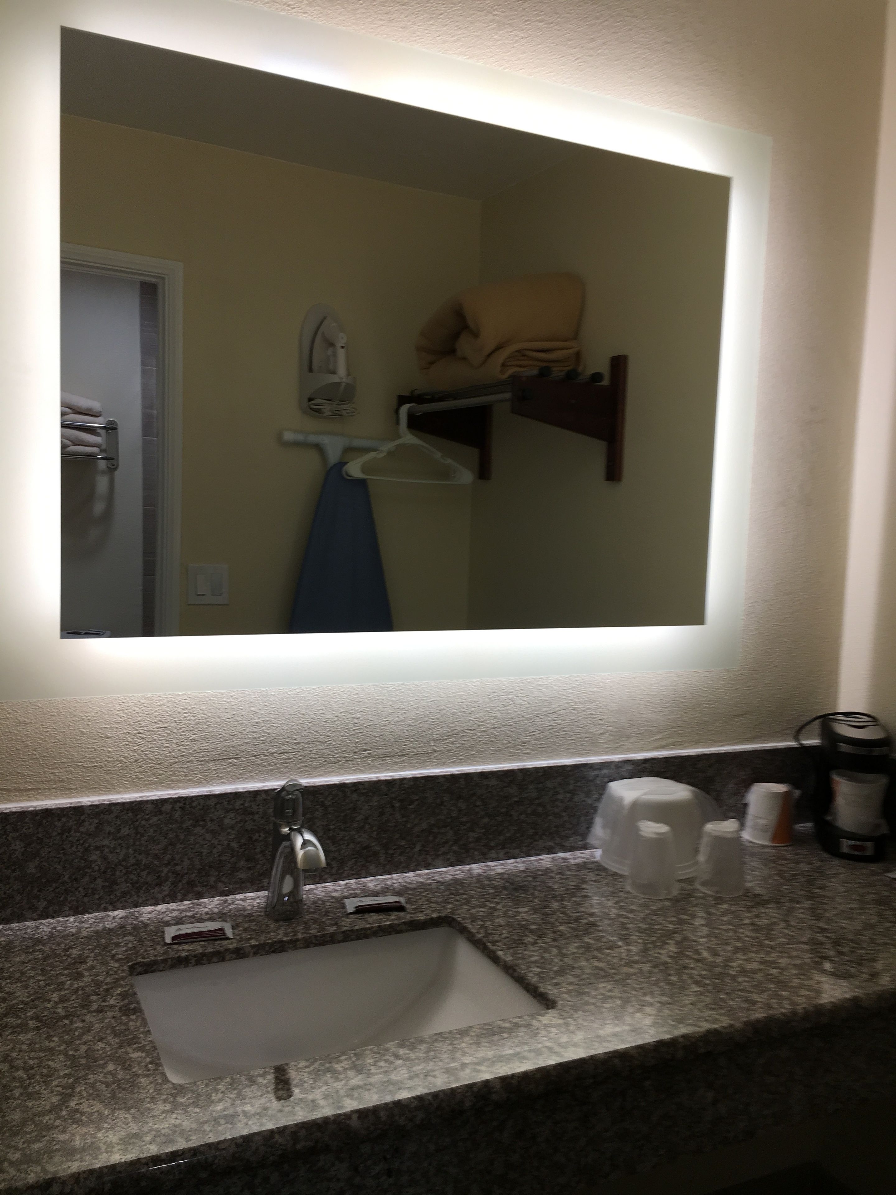 Un baño con encimera de granito, un lavabo, un espejo y un perchero para toallas.