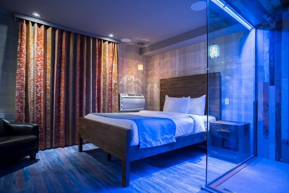 A modern hotel room with a wooden bed, a glass partition, and a built-in air conditioning unit.