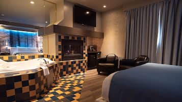 Una habitación de hotel con piso a cuadros, una cama grande, una chimenea, un televisor y vistas a árboles por la ventana.