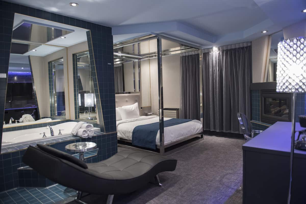 Una habitación de hotel moderna con una cama grande, un baño independiente con bañera, una zona de estar y un espejo amplio.