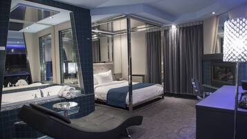A modern hotel room with a large bed, a separate bathroom with a bathtub, a sitting area, and a large mirror.