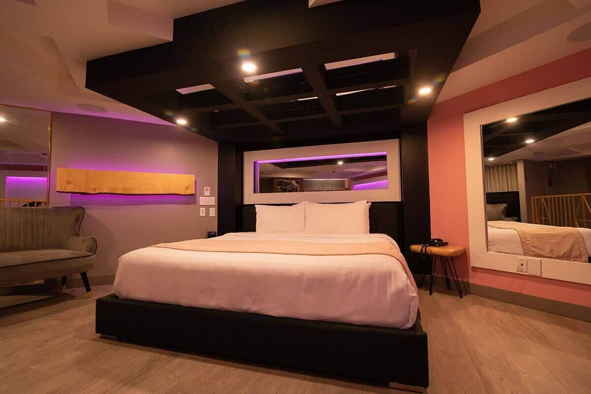 Un dormitorio moderno con una cama grande, un sofá, una mesita y un espejo.