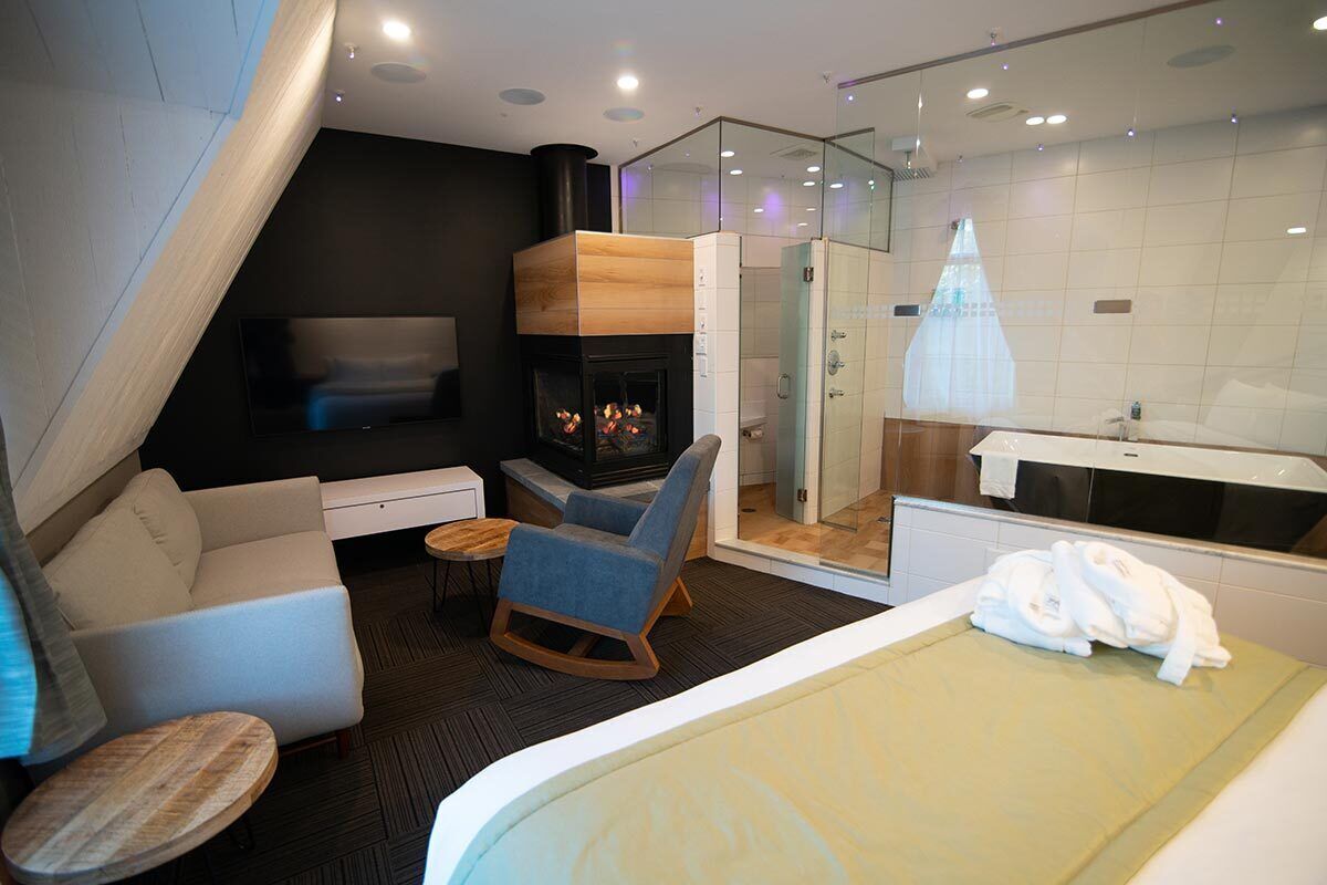 Una habitación de hotel moderna con chimenea, una zona de estar con sofá y sillones, cabina de ducha de vidrio y bañera.