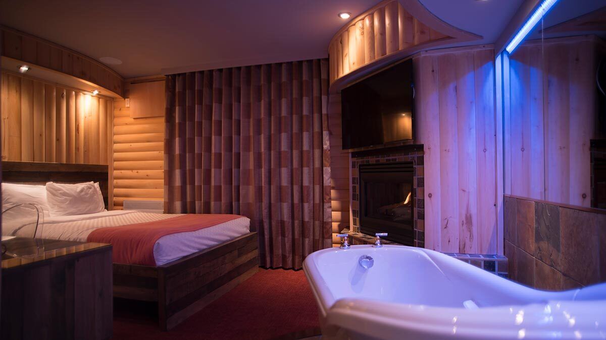 Une chambre confortable, aménagée dans le style d’un chalet en rondins, avec un lit, une grande baignoire et une cheminée.