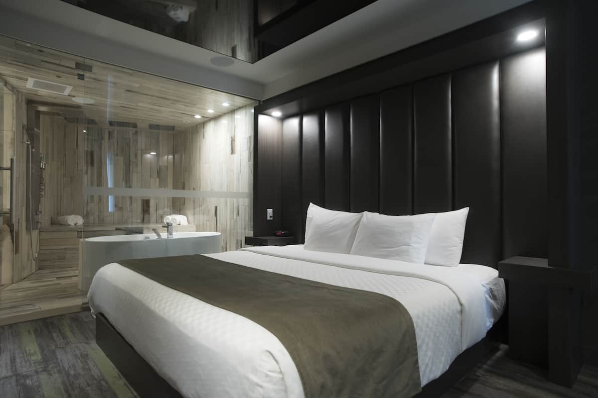 Una habitación de hotel moderna con una cama grande, un baño con bañera y un vestidor.