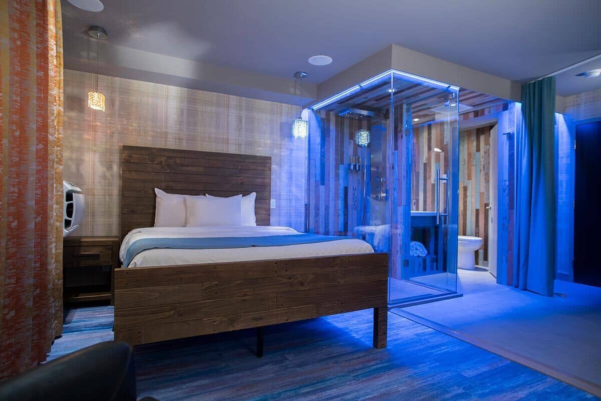 Una habitación de hotel moderna con una cama de madera, un box de ducha con mampara de vidrio y vistas al baño.