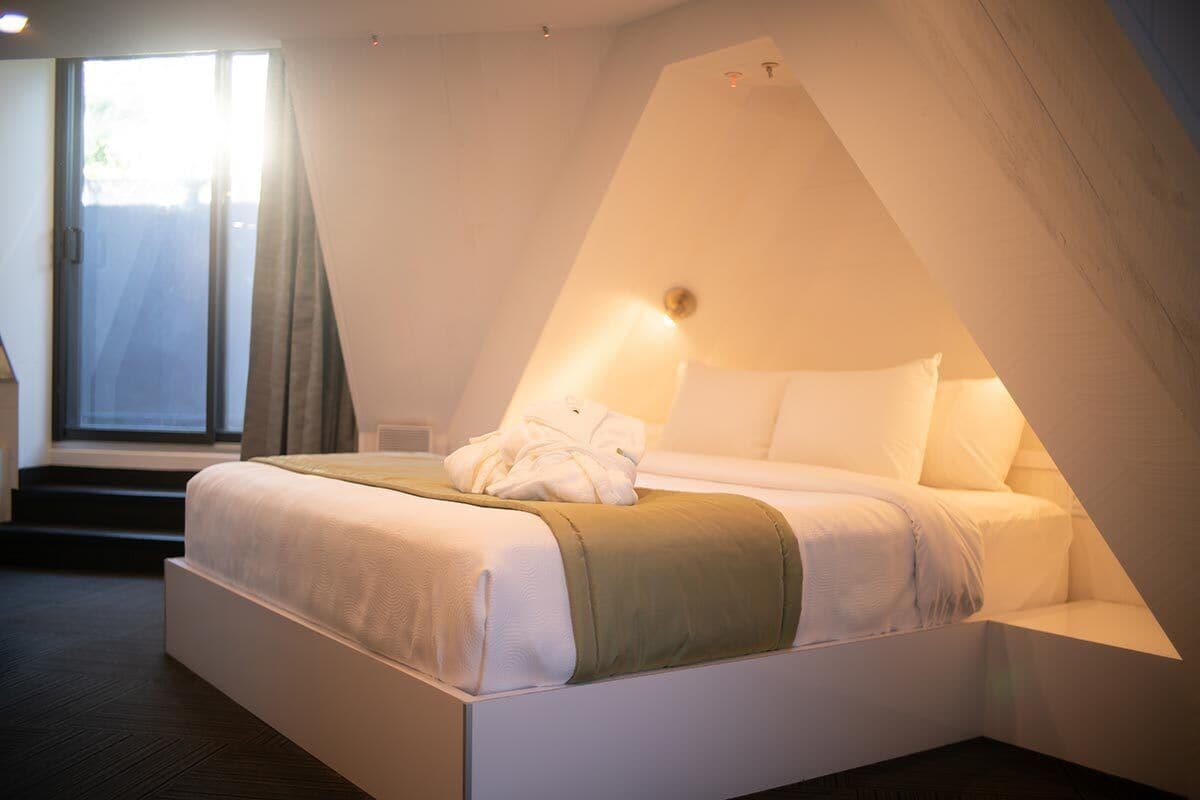 Un dormitorio moderno con cama, ventana y un diseño de techo inclinado original.