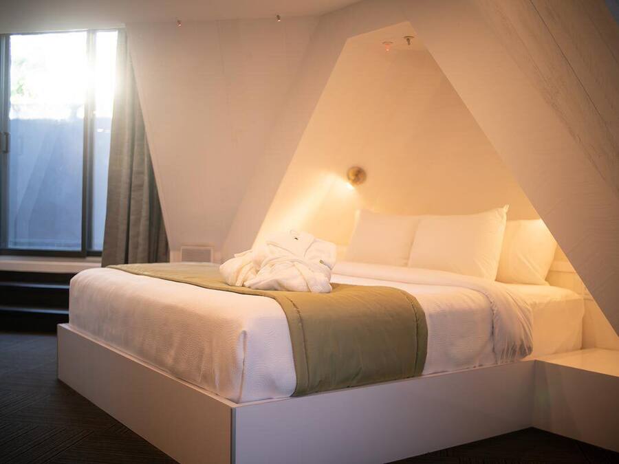 Un dormitorio moderno con cama, ventana y un diseño de techo inclinado original.