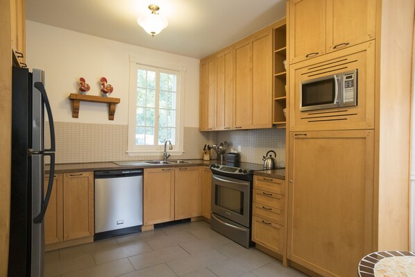 A kitchen with wooden cabinets, stainless steel appliances, and a window with a view of trees.