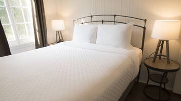 A neatly made bed with white linens, a metal headboard, and two bedside lamps on wooden stands.