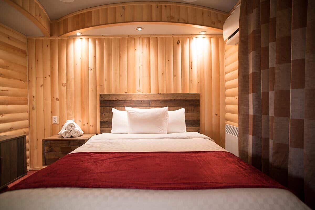 Una habitación acogedora estilo cabaña de madera con una cama, una mesita de noche y una manta roja.