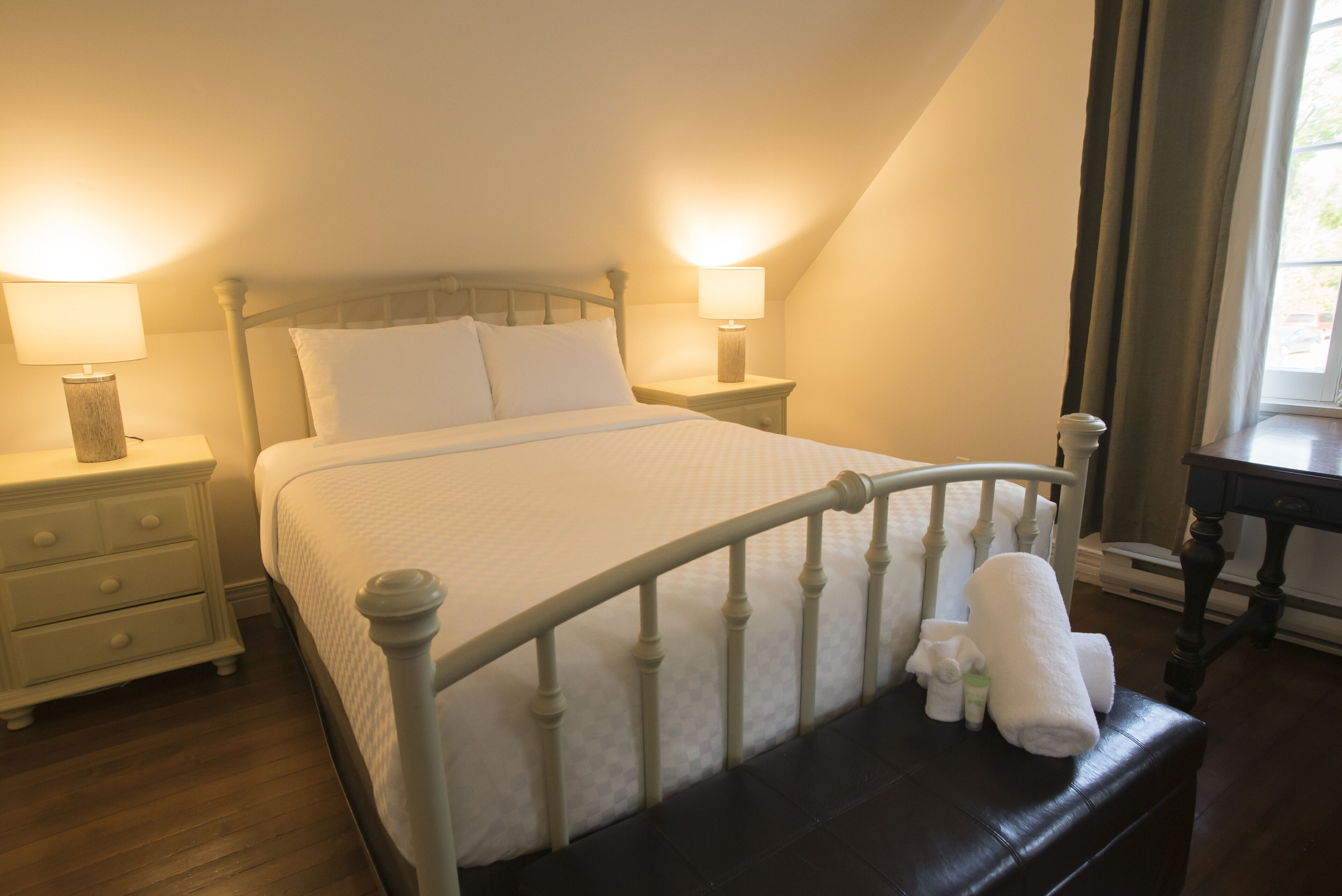 A neatly made bed with white linens, a wooden headboard, and two bedside lamps.