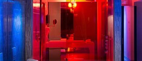 Un baño moderno con un lavamanos grande de color blanco, cabina de vidrio e iluminación ambiental roja.