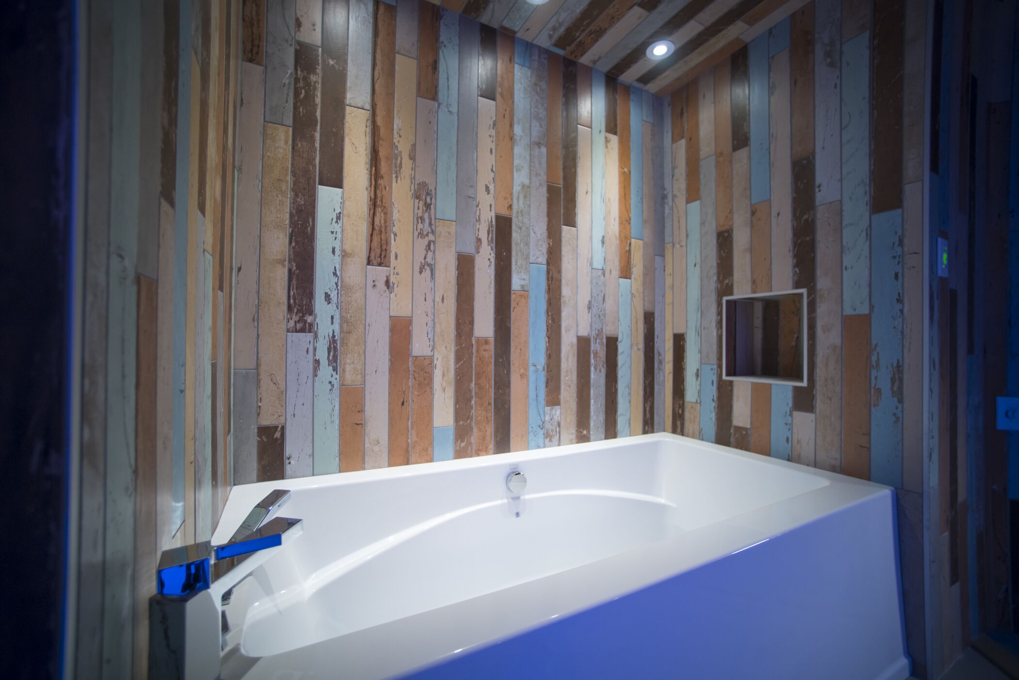 Un baño moderno con una bañera blanca grande, paneles de madera y un espejo pequeño.