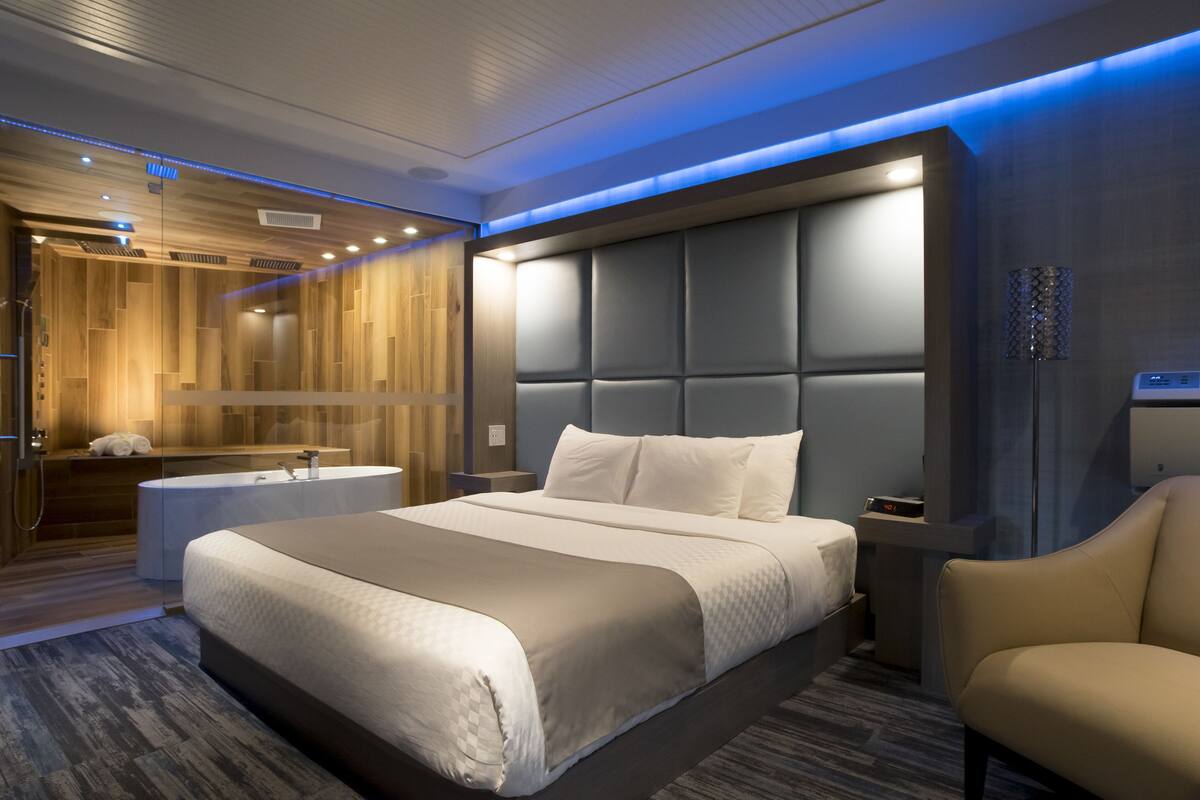 Una habitación de hotel moderna con una cama grande, baño independiente y zona de estar.
