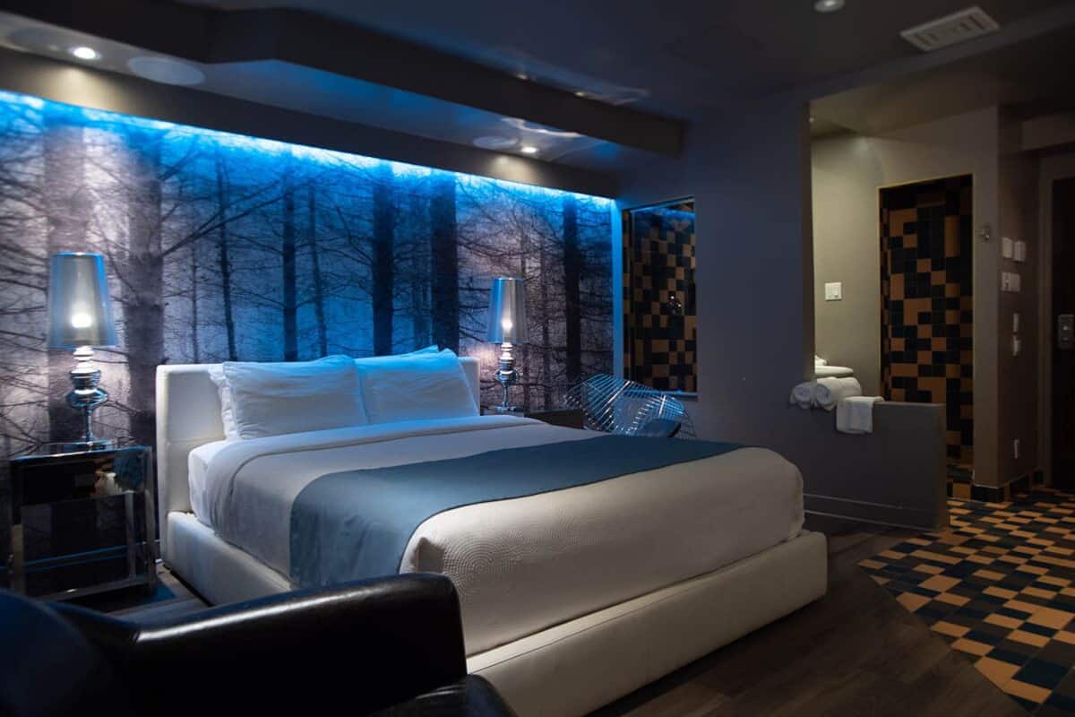 Un dormitorio moderno con una cama grande, una mesita de noche, una silla y un televisor montado en la pared.