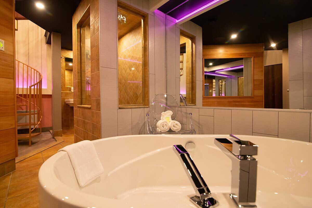 Ein modernes Badezimmer mit einer großzügigen Badewanne, Holzelementen und einem Spiegel, der den Raum widerzuspiegeln scheint.