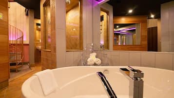 Un baño moderno con una bañera grande, detalles de madera y un espejo que refleja la habitación.
