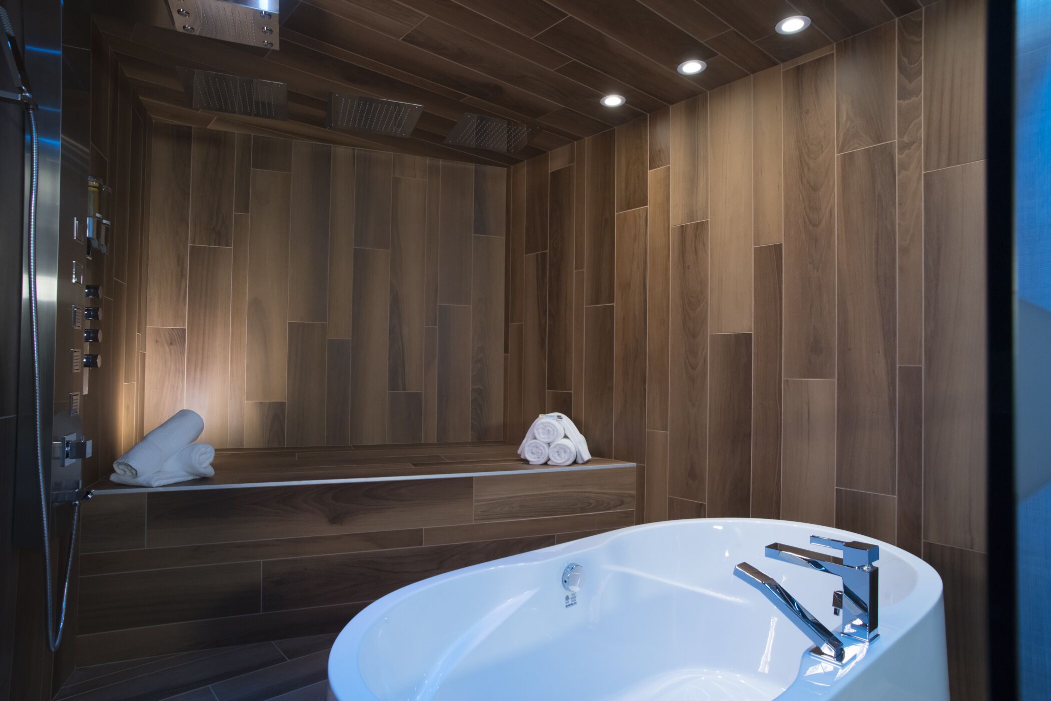A modern bathroom with a freestanding bathtub, wooden panel walls, and built-in towel racks.